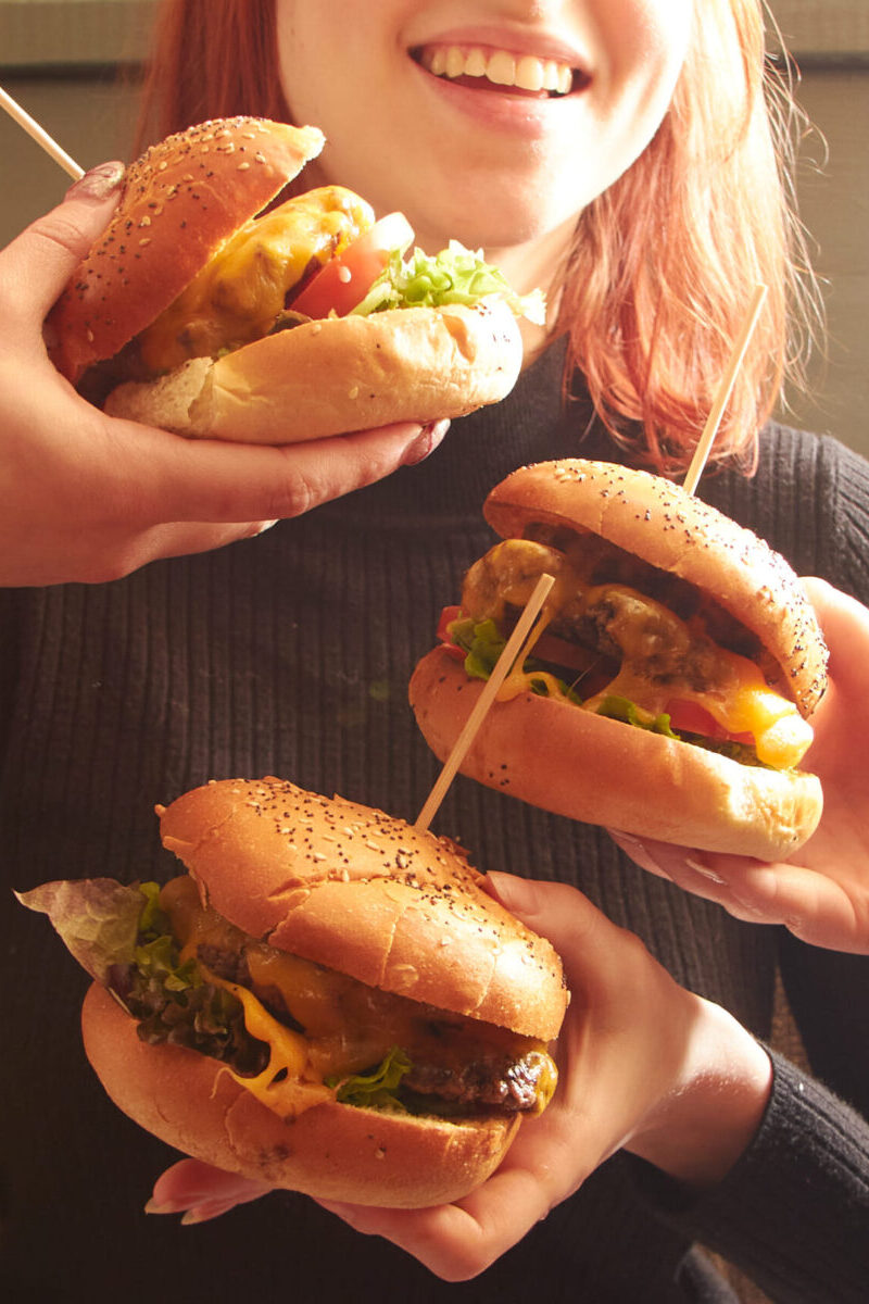 A girl with three burgers in front of her.