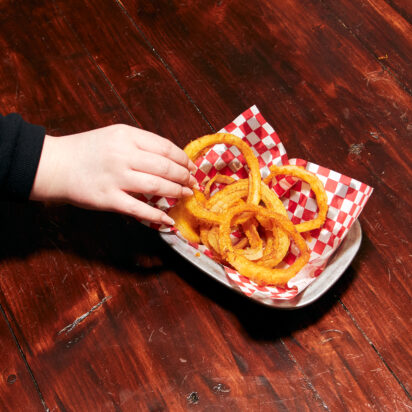 A hand grabbing towards onion rings.