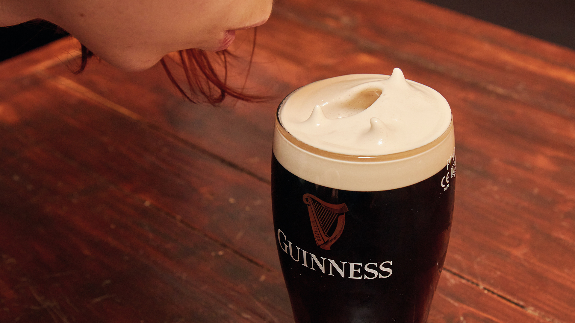 A girl blowing softly into her pint.