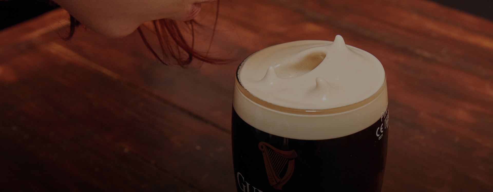 A girl blowing softly into her pint.