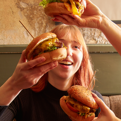Three hamburger held in front of a girl.