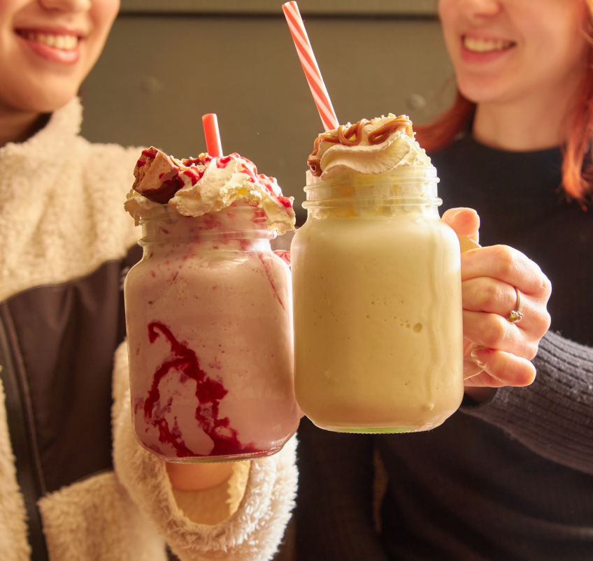 Two girls cheersing a milkshake.